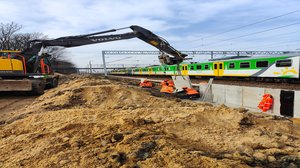 Prace modernizacyjne na przystanku Mińsk Mazowiecki. Koparka, obok przejeżdżający pociąg.
