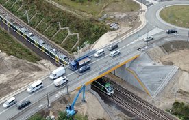 Widok z góry na pociąg jadący po torze pod nowym wiaduktem drogowym w Warce